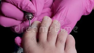 美甲师傅戴着粉色手套，在美甲沙龙用钻头割去角质层和虫胶趾甲。专业修脚